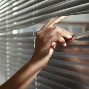 A woman peeping through venetian blinds